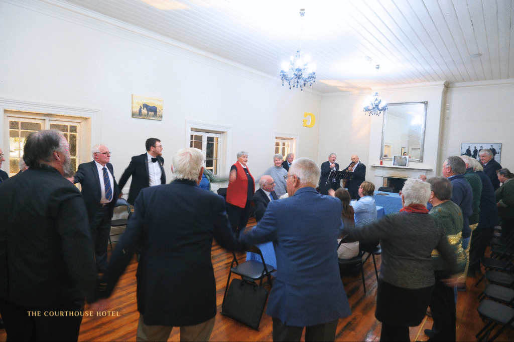 Guests standing in a circle enjoying live music in the upstairs function room at The Courthouse Hotel Smythesdale, with timber floors, high white ceilings and chandeliers.